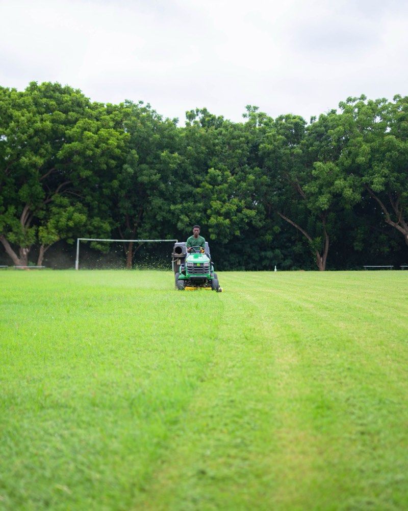 A ride-on mower cutting neat stripes across a wide green lawn