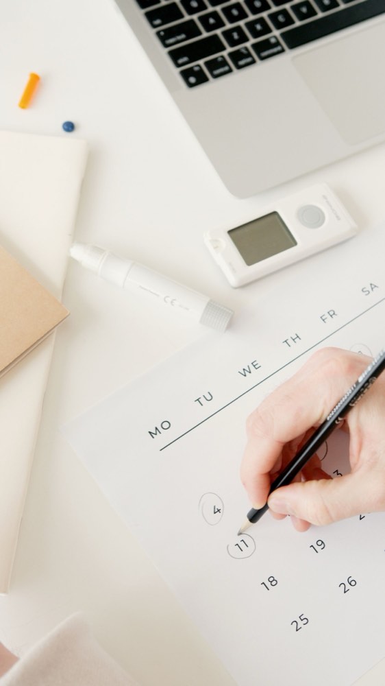 A hand marking dates on a calendar beside a laptop