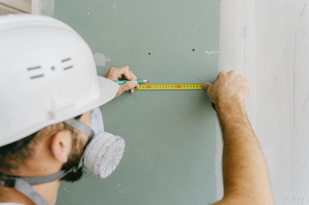 A worker in a hard hat measuring a wall during a building improvement