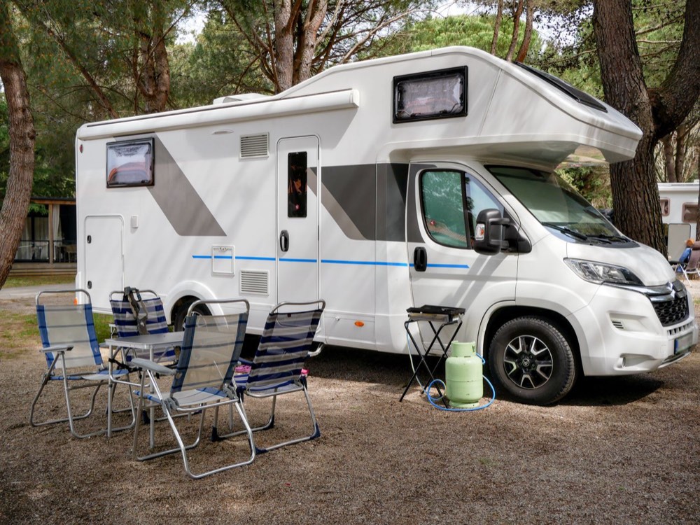 A motorhome set up on a campsite with folding chairs and a table outside
